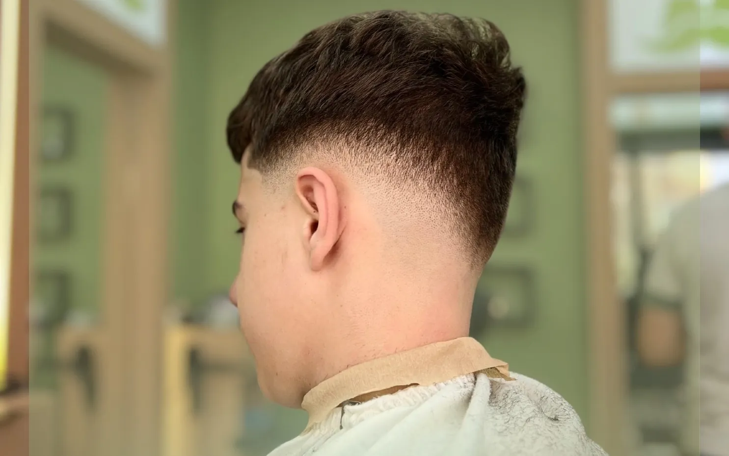 A fresh low fade in the Mustaqe chair, sage arches behind